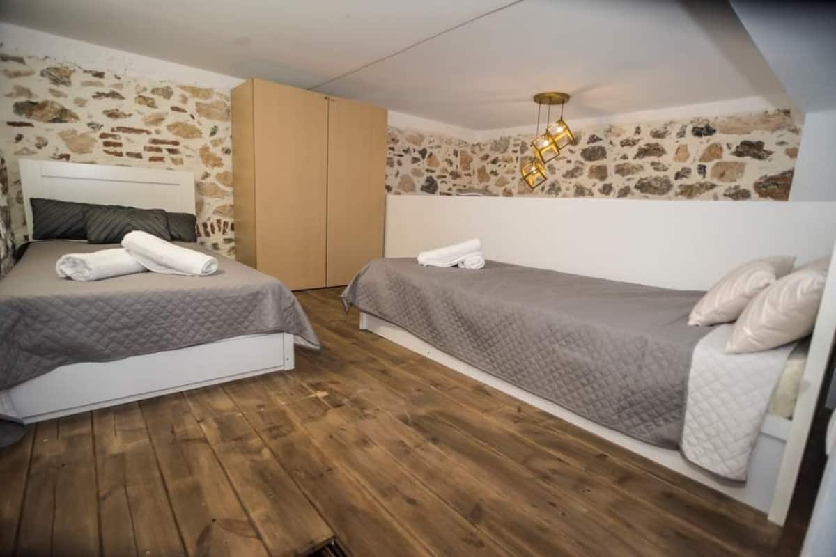Une chambre avec deux lits, un plancher en bois, des murs en pierre et un luminaire suspendu.