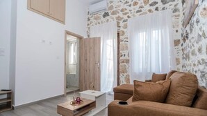 Una sala moderna con pared de piedra, un sofá marrón, una mesa de centro de madera y una mesita auxiliar blanca.