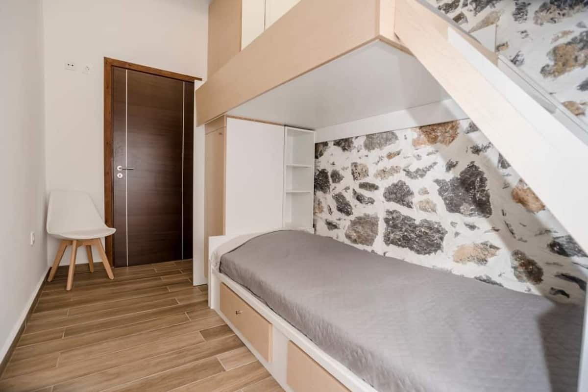 Une petite chambre à coucher avec un lit superposé, une chaise blanche et une porte.