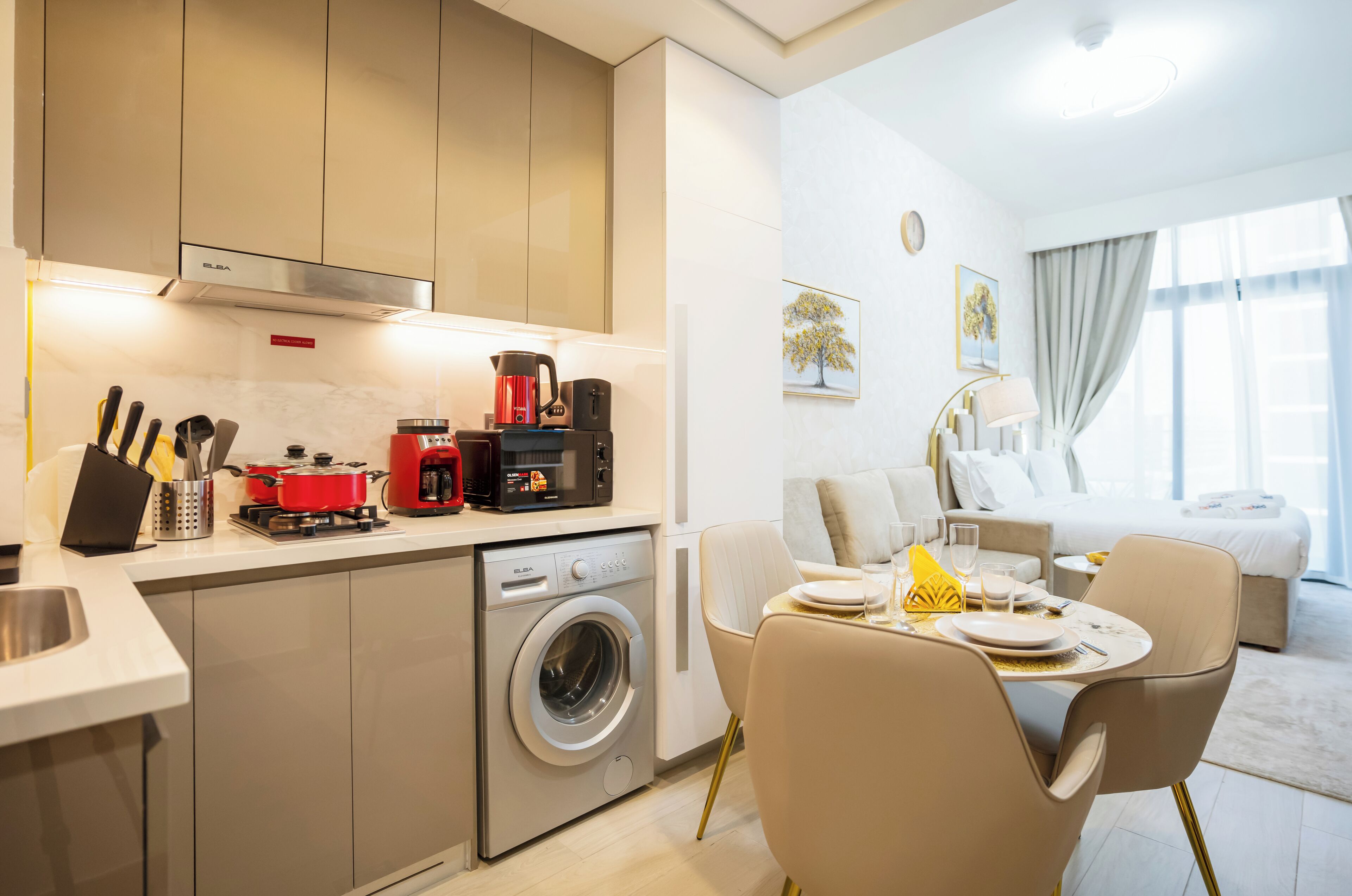 A modern kitchen with a washing machine, a coffee maker, and a dining area with a table set for two.