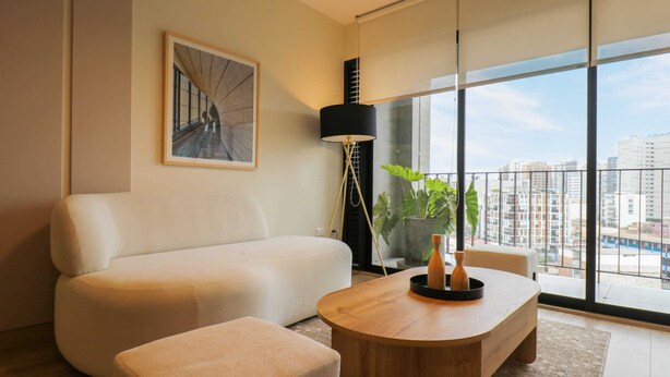 A modern living room with a sofa, a coffee table, a floor lamp, and a large window with a city view.