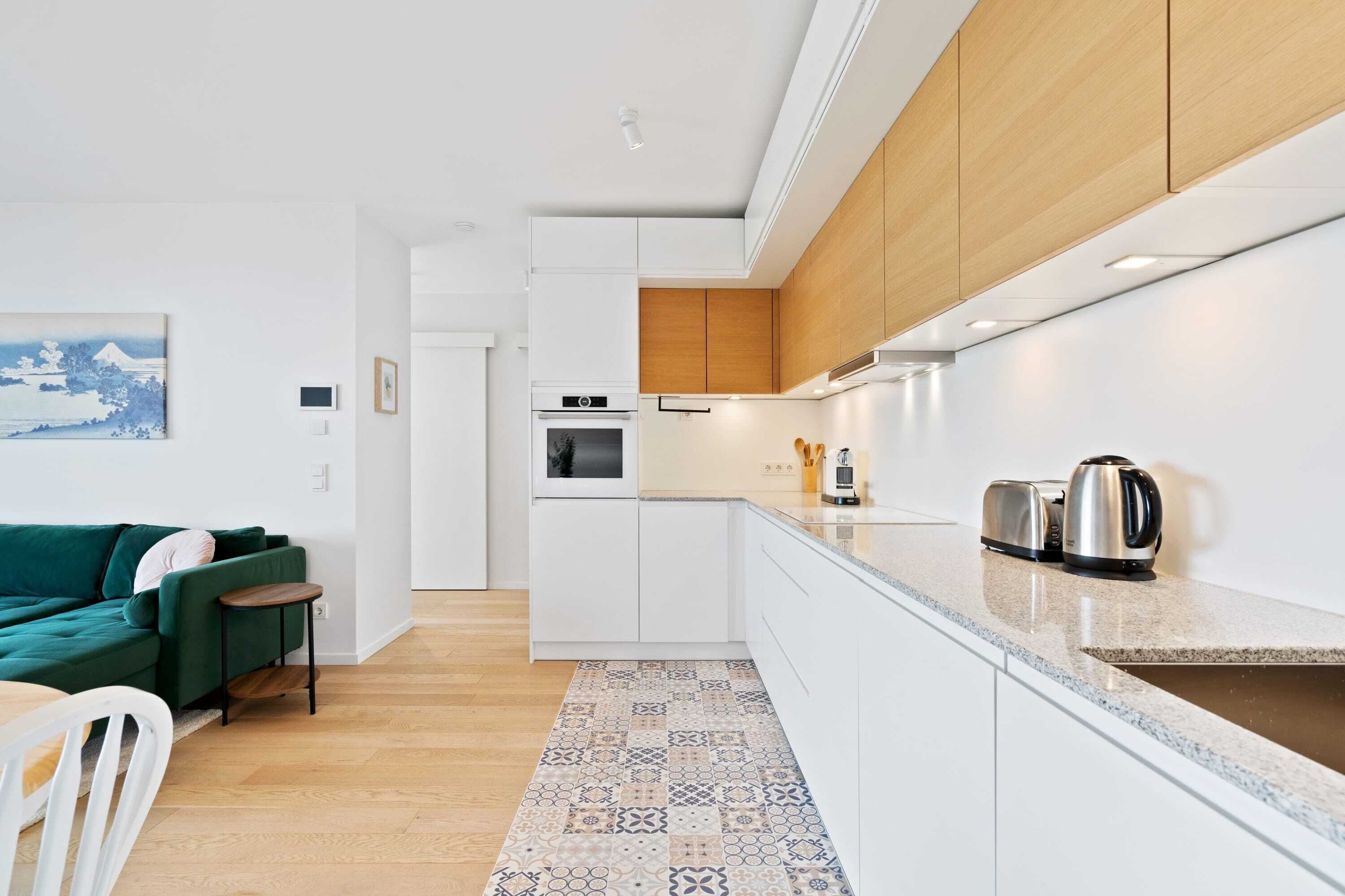 A modern kitchen with white cabinets, a wooden countertop, and a patterned rug.
