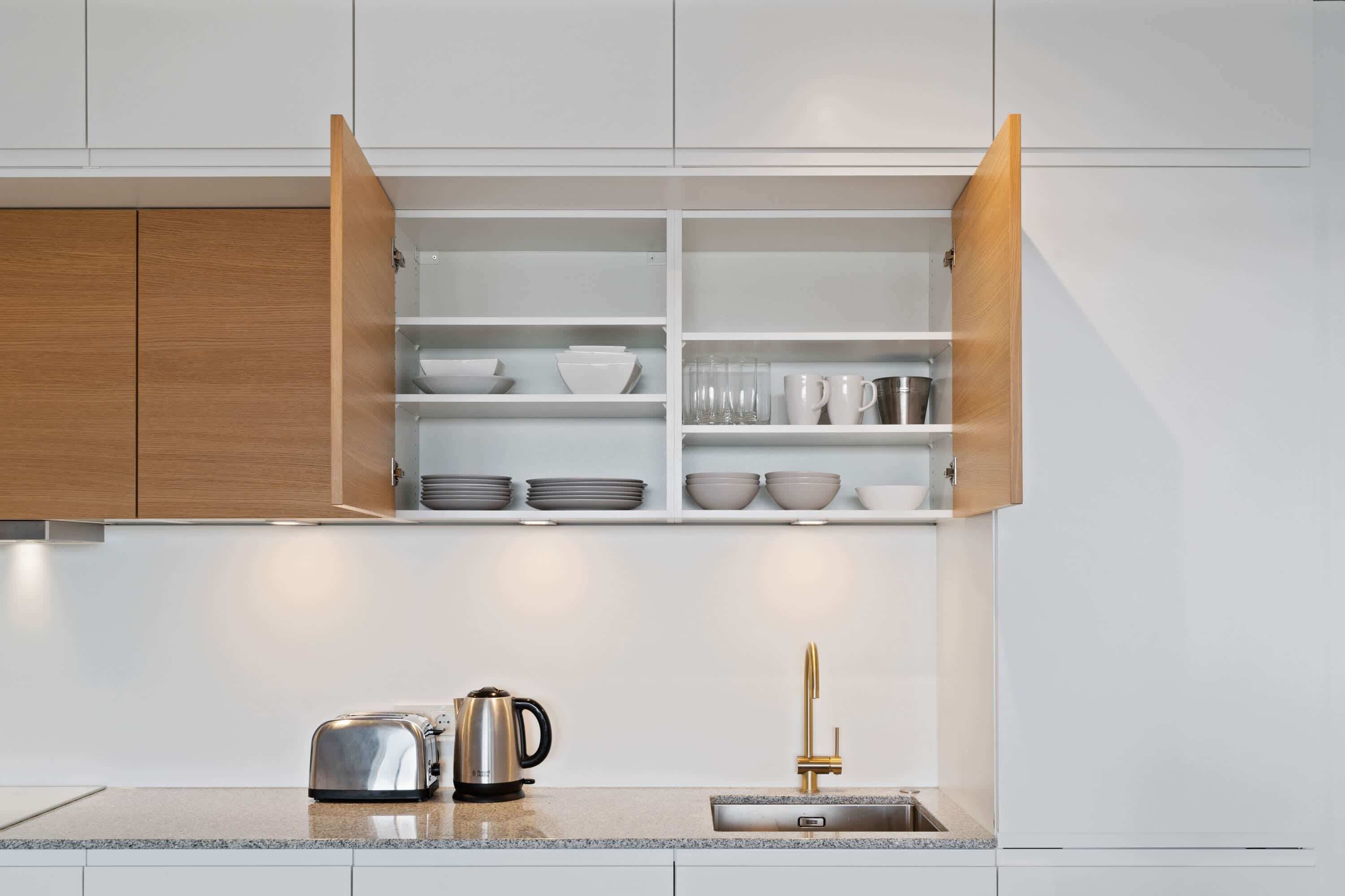 Een moderne keuken met open houten kastjes, een roestvrijstalen broodrooster en een gouden kraan.