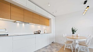 Cuina moderna amb armaris blancs, taulell de fusta i zona de menjador amb taula rodona i cadires blanques.