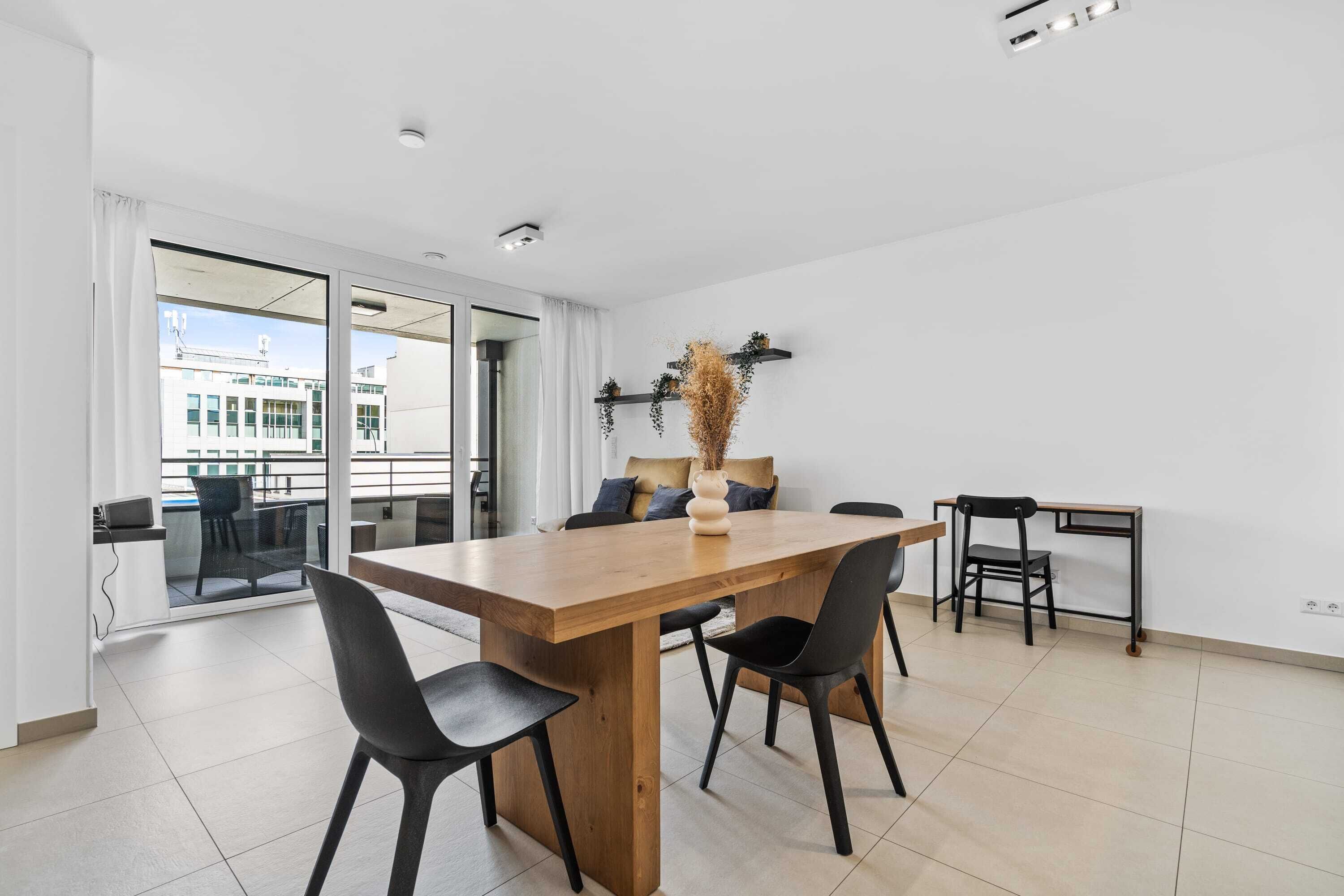 A modern dining area with a wooden table, black chairs, and a view through large glass doors.