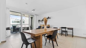 A modern dining area with a wooden table, black chairs, and a view through large glass doors.