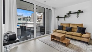 A modern living room with a sofa, coffee table, and a view through large glass doors to an outdoor balcony.