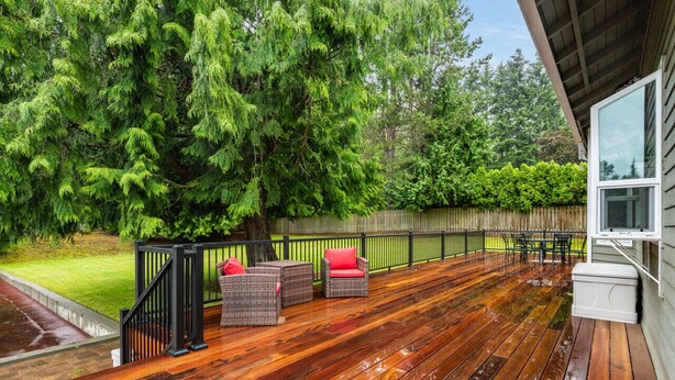 Una terraza de madera con mobiliario de mimbre y barandilla negra.