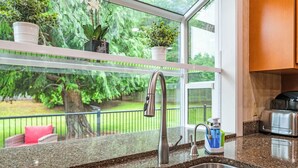 Una cocina con un lavamanos de acero inoxidable, una ventana con vistas a la vegetación y un tostador en la encimera.