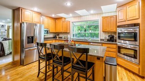 Una cocina moderna con armarios de madera, electrodomésticos de acero inoxidable y una zona de bar con taburetes.
