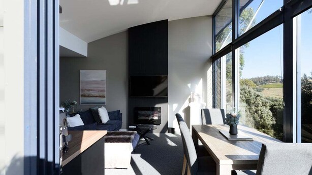 Un salon moderne comprenant un canapé, une table basse et un coin repas, de grandes fenêtres et une cheminée.