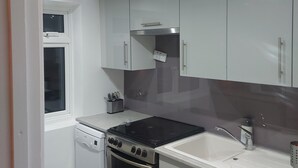 Una cocina moderna con armarios blancos, una estufa negra, horno integrado, un lavaplatos y una ventana sobre el lavaplatos.