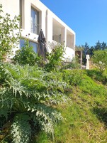 Um edifício branco com varandas, cercado por vegetação exuberante e um céu azul límpido.