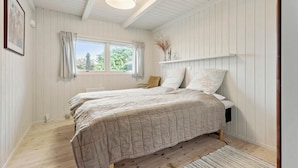 Ein Schlafzimmer mit zwei Betten, einem Fenster, einer Deckenleuchte und einem Regal mit Dekoration.