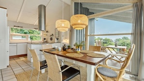 Eine moderne Küche mit einer großen Kochinsel, hängenden Rattanleuchten und Blick auf den Garten durch große Fenster.