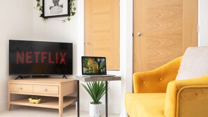 Ein modernes Wohnzimmer mit einem Holz-TV-Schrank, einem gelben Sessel, einem kleinen Beistelltisch mit einem Laptop und einer Topfpflanze.