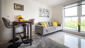 Ein modernes Wohnzimmer mit grauem Sofa, gelben Kissen, einem Couchtisch mit Frühstücksutensilien und Kunstwerken an den Wänden.