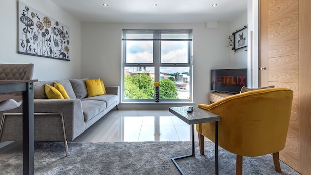 Ein modernes Wohnzimmer mit einem grauen Sofa, gelben Kissen, einem Couchtisch und einem Fernseher, der das Netflix-Logo zeigt.