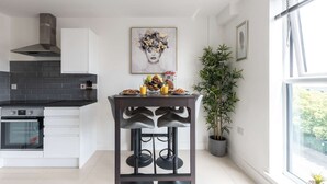 Una cucina moderna con zona pranzo, caratterizzata da un piano cottura in acciaio inossidabile, un bancone nero e un tavolo con una ciotola di frutta e una cornice con un'immagine sopra.