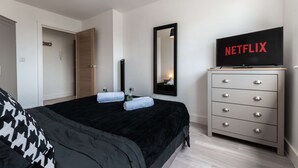 Una moderna camera d'albergo con un letto grande, una cassettiera, uno specchio e un televisore che mostra 'NETFLIX'.