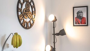 Une table à manger avec des aliments pour le petit-déjeuner, un panier de fruits, une horloge et une lampe.