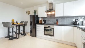 A modern kitchen with white cabinets, a black refrigerator, a built-in oven, and a coffee machine.
