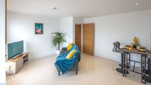 A modern living room with a sofa, a dining table with chairs, a potted plant, and a painting on the wall.