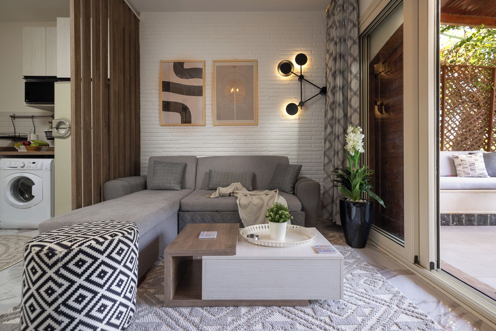 Una sala de estar moderna con un sofá seccional gris, un cojín estampado, una mesa de centro y una lámpara de pared.