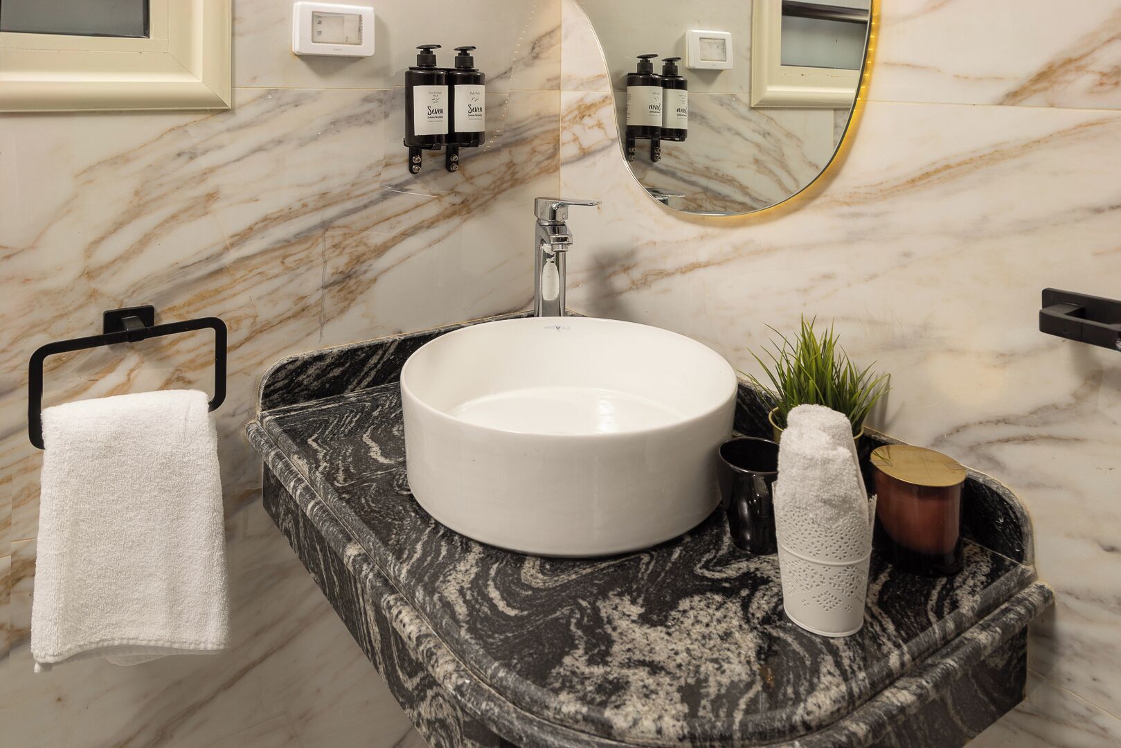 A bathroom with a marble sink, a towel rack, a mirror, and toiletries.
