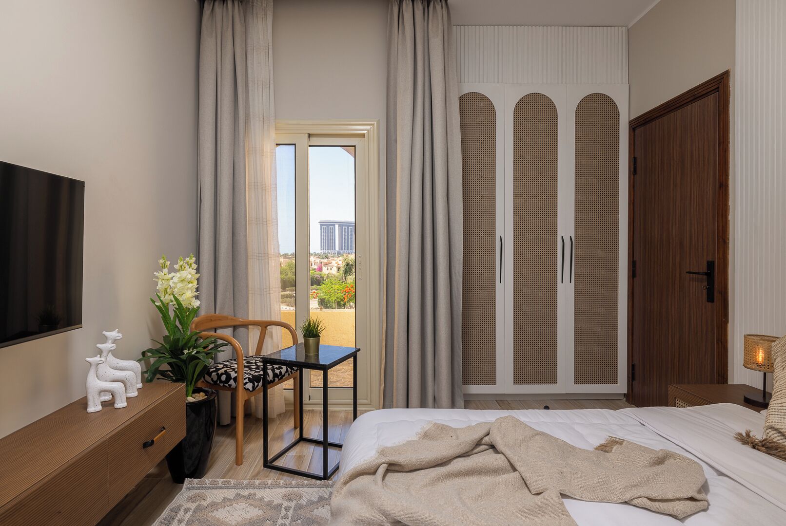A bedroom with a bed, a desk, a chair, a TV, and a sliding door with a view.