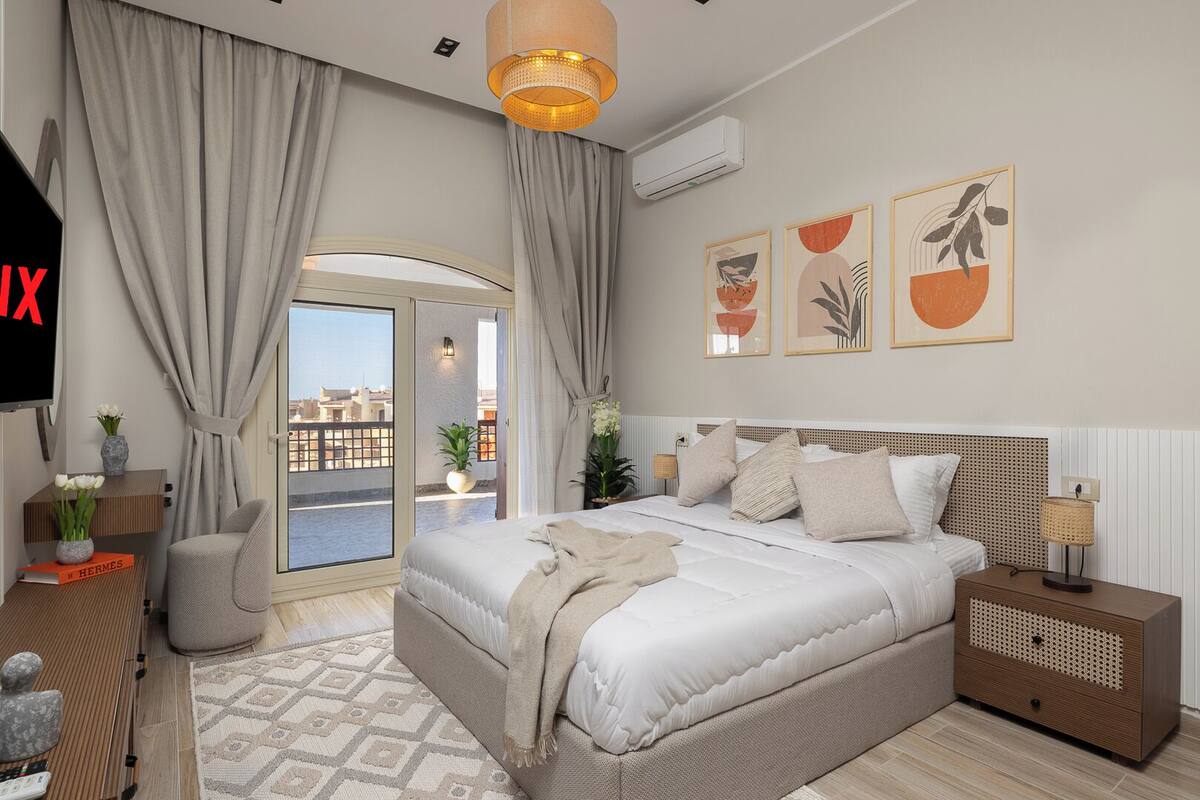 Un dormitorio moderno con una cama grande, una mesita de noche, una lámpara de pie y vistas de la ciudad a través de una puerta corredera.