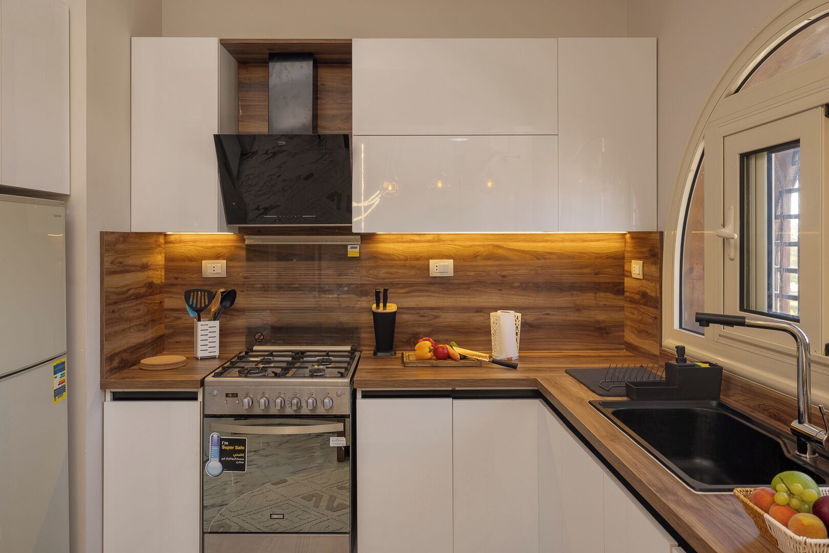 A modern kitchen with white cabinets, a wooden backsplash, a gas stove, and a sink.