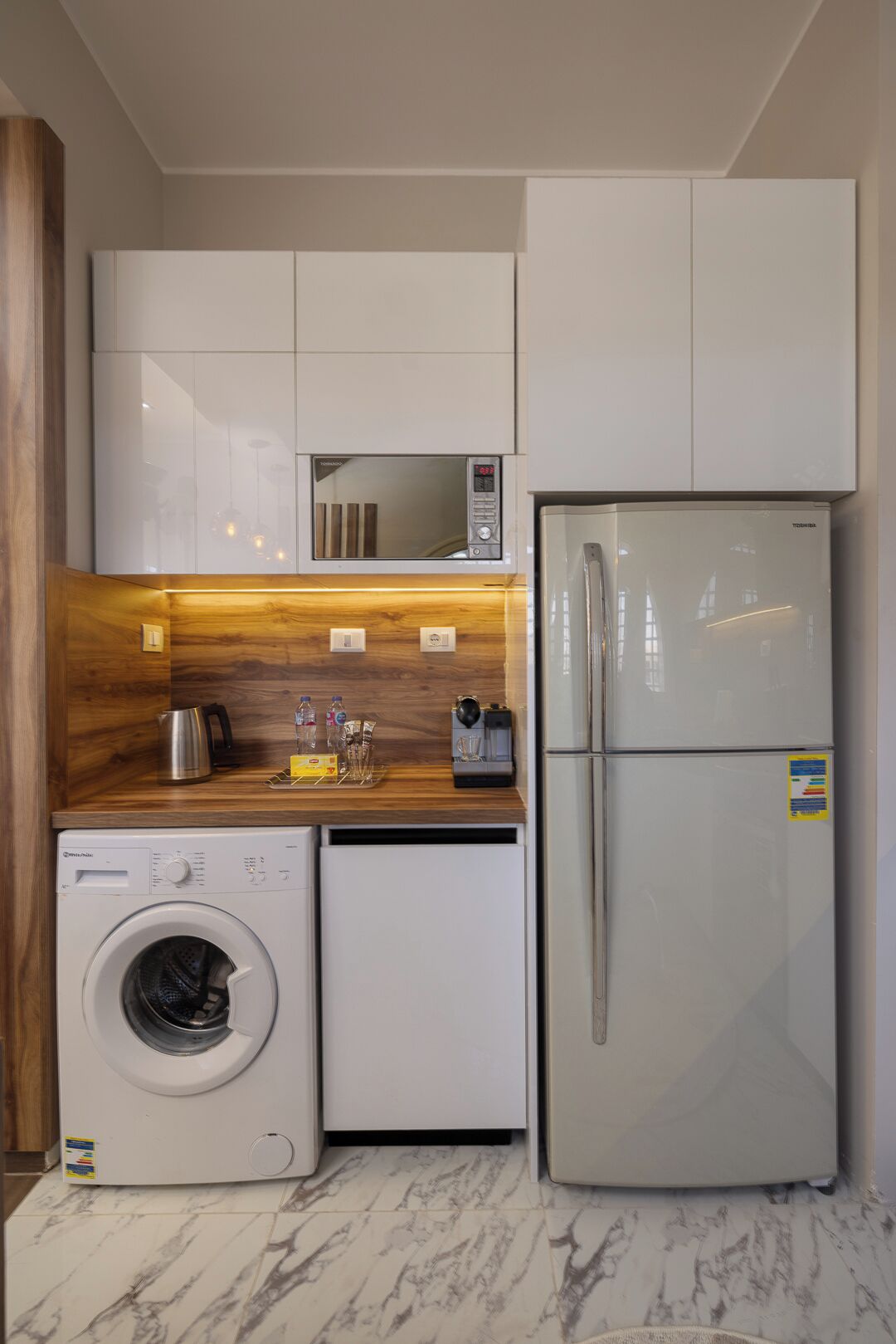 A compact kitchen with a washing machine, a refrigerator, and a microwave.
