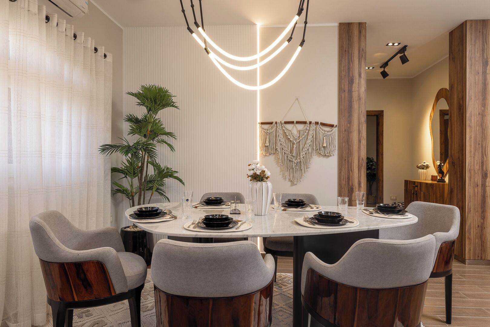 A modern dining room with a round table, grey upholstered chairs, and a central light fixture.