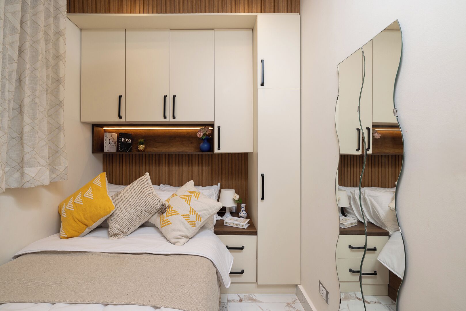 Quarto com cama, mesas de cabeceira, espelho e guarda-roupa.