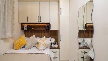 Quarto com cama, mesas de cabeceira, espelho e guarda-roupa.