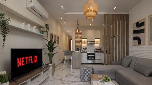 A modern living room with a flat-screen TV, a sofa, a coffee table, and a dining area with a chair. - Marina Resort By Seven Seasons (Al-Hammam)