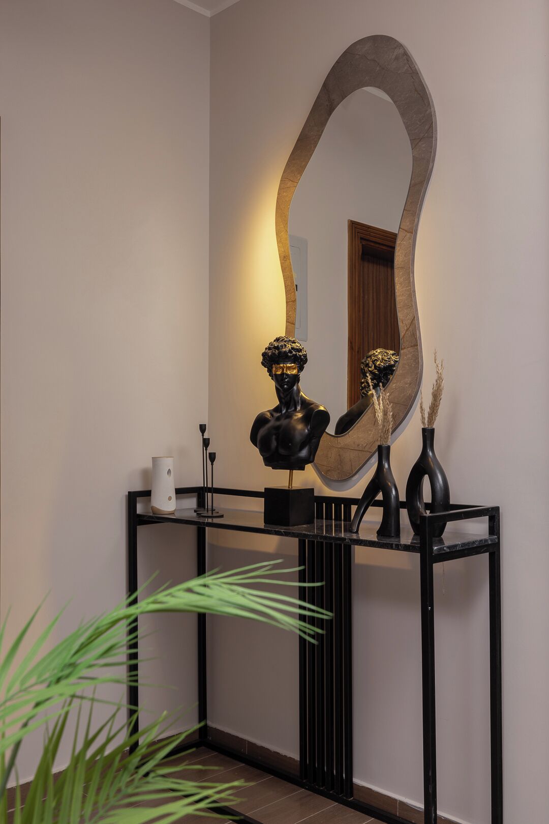 Une console surmontée d’un miroir, agrémentée d’un buste sculpté et de deux vases.