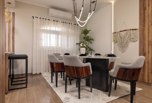 A dining area with a round table, four chairs, a plant, and a macrame wall hanging.