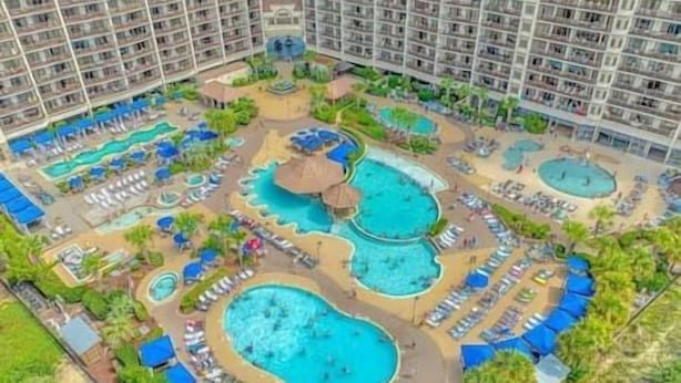 Ein Hotel mit mehreren Schwimmbecken, Liegestühlen und einer zentralen Fontäne.