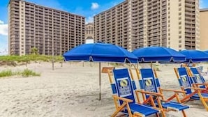 Ein Strand mit Reihen von blauen Liegestühlen und Sonnenschirmen, im Hintergrund hohe Wohnhäuser.