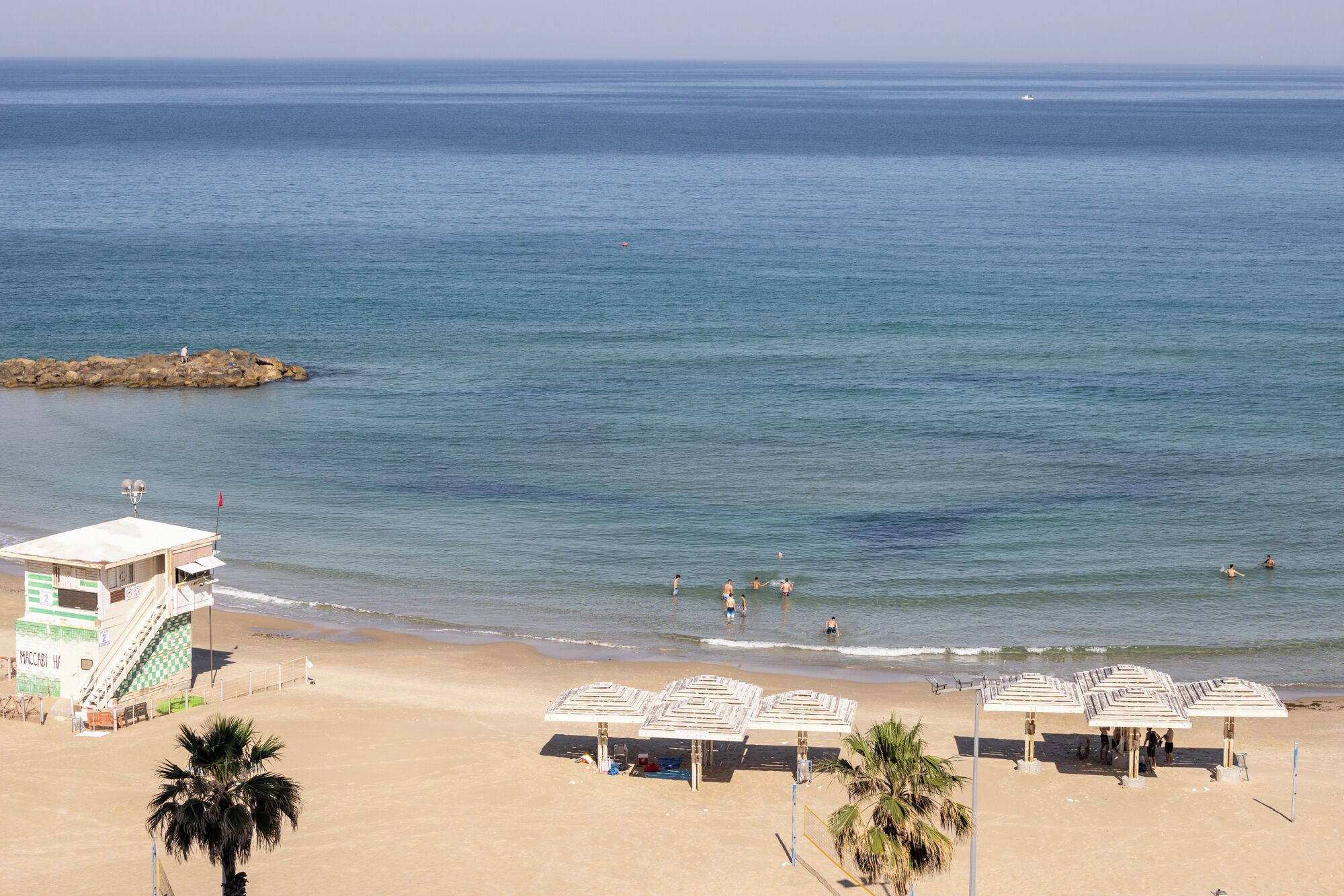 Une plage avec une tour de surveillance, des parasols et un affleurement rocheux dans l’eau.