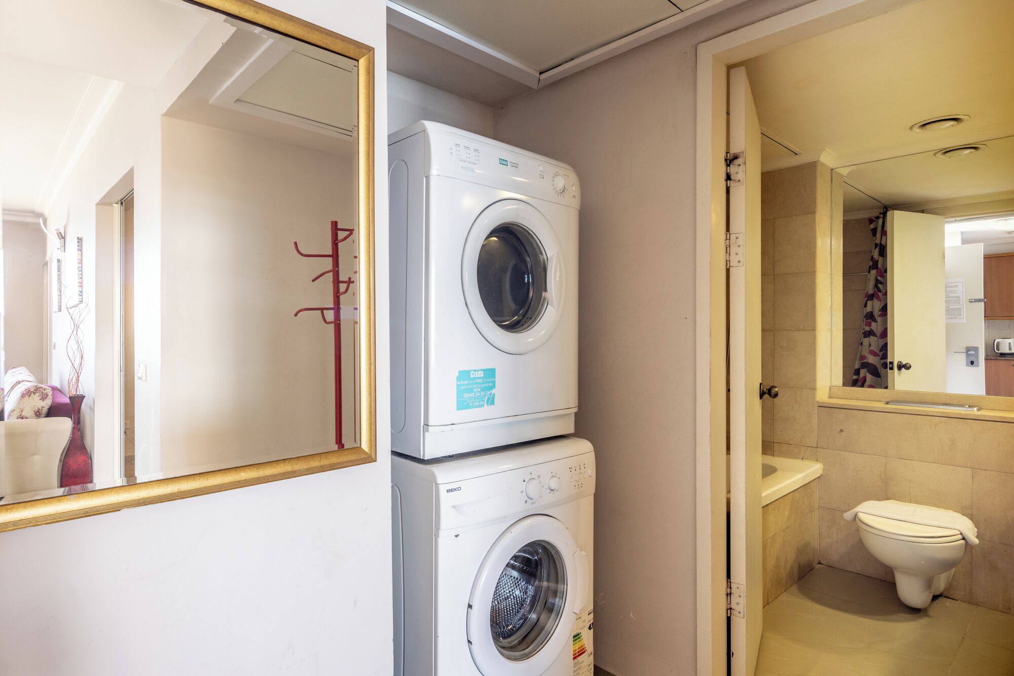 A compact bathroom with a washing machine, toilet, and a mirror.