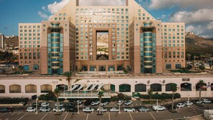 A large hotel with a central atrium, multiple floors, and a parking lot. - Carmel Seaside Sunny Stays by Sea N Rent (Haifa)