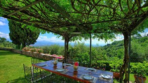 Un espace de restauration en plein air avec une table dressée pour deux personnes, entouré d’une végétation luxuriante et d’un mur de pierre.