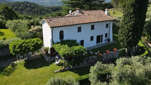 Une villa blanche, dotée d’un toit en tuiles, entourée d’une végétation luxuriante et d’un mur de pierre.