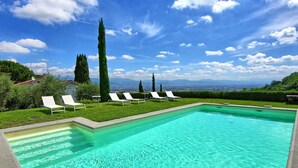 Une piscine rectangulaire à l’eau turquoise et limpide, entourée de chaises longues blanches et d’une pelouse bien entretenue.