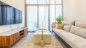 Una sala de estar moderna con una televisión de pantalla plana, una mesa de centro de mármol, un sofá y un ventanal con cortinas traslúcidas.