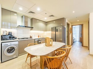 A modern kitchen with a built-in washing machine, a refrigerator, and a dining area with wooden chairs.