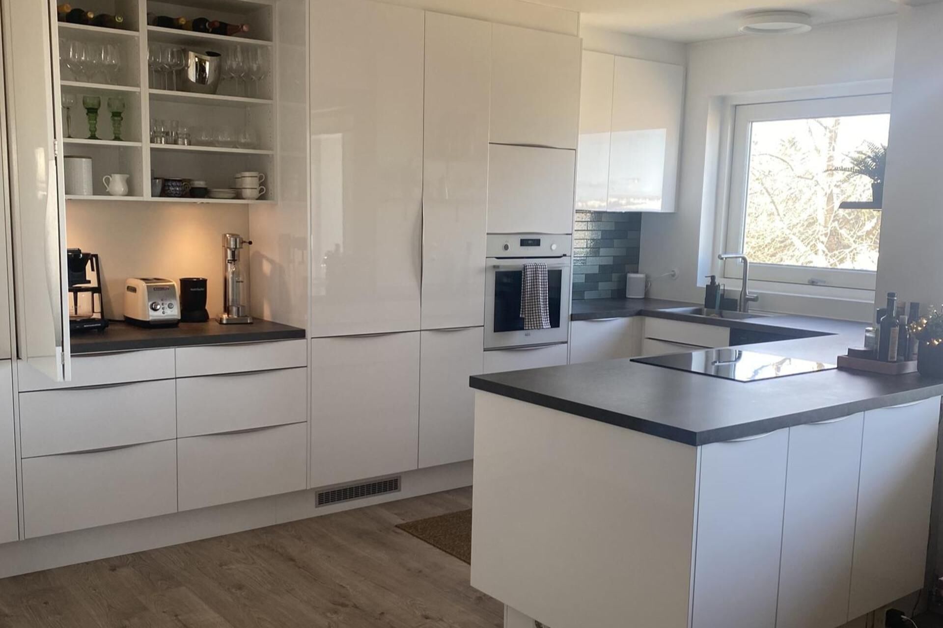 Uma cozinha moderna com armários brancos, uma ilha central e um forno embutido.